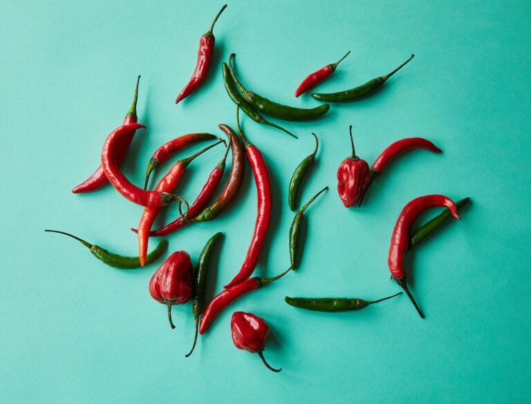 From above of red and green various chili peppers scattered on blue background